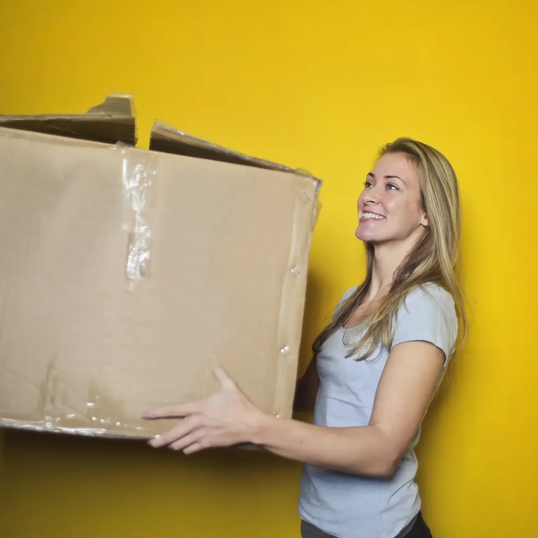 Mujer sonriente sosteniendo una caja de cartón sobre un fondo amarillo