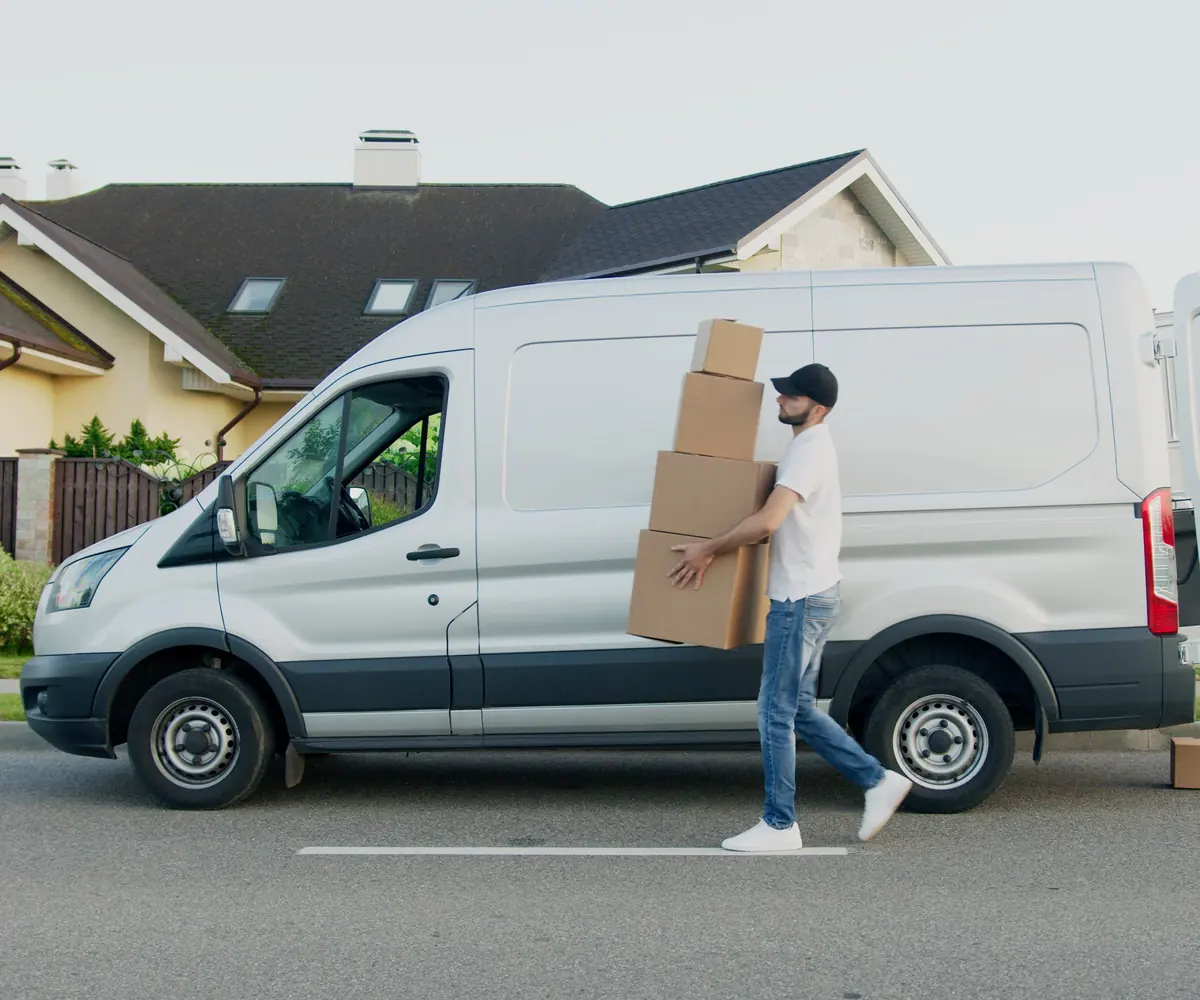 Repartidor cargando cajas junto a una furgoneta frente a una casa