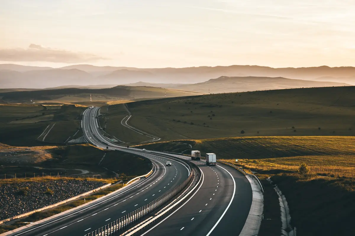Carretera al atardecer con camiones en la distancia